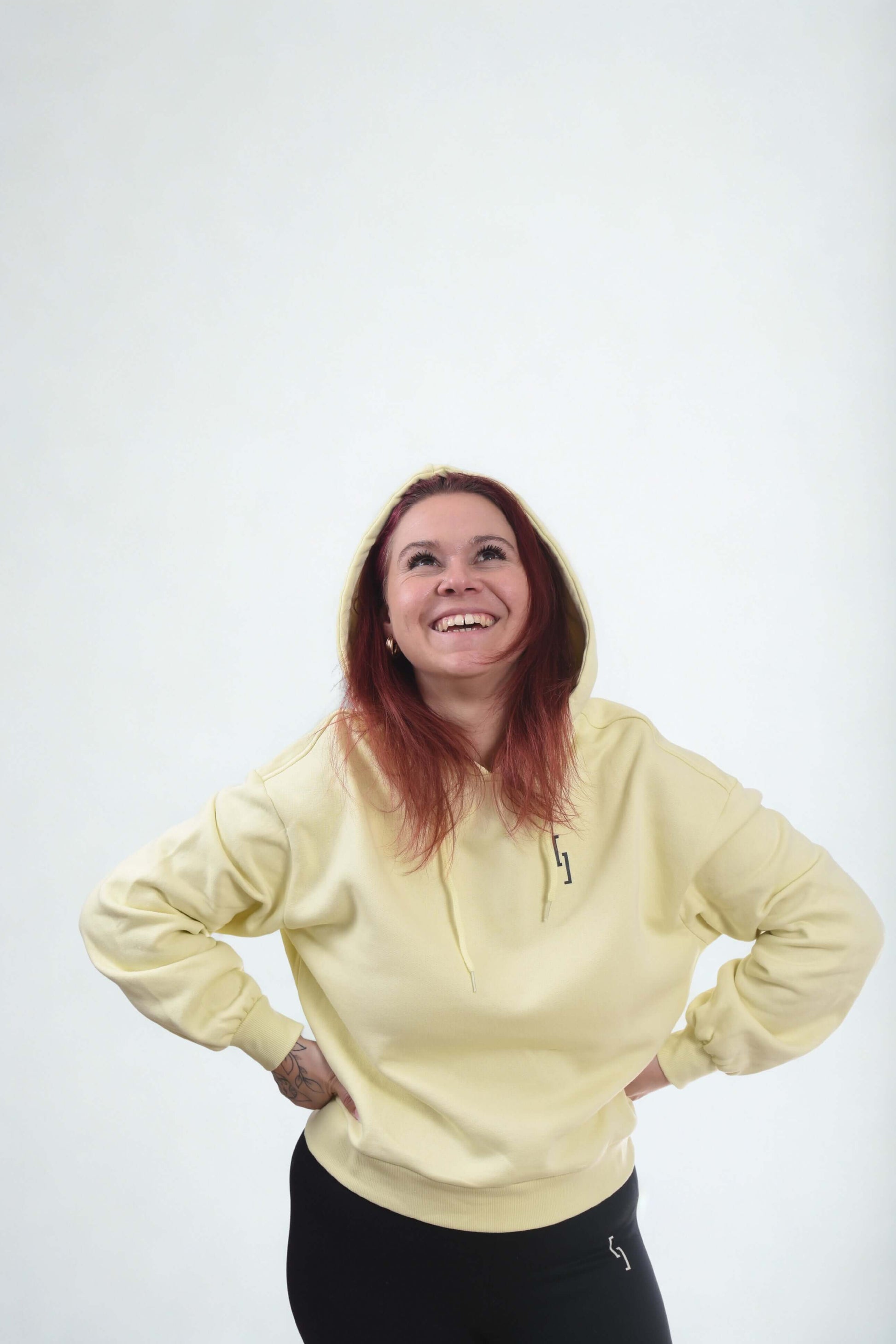 Cropped oversized hoodie in pastel yellow worn by smiling woman with red hair, showcasing comfort and style.