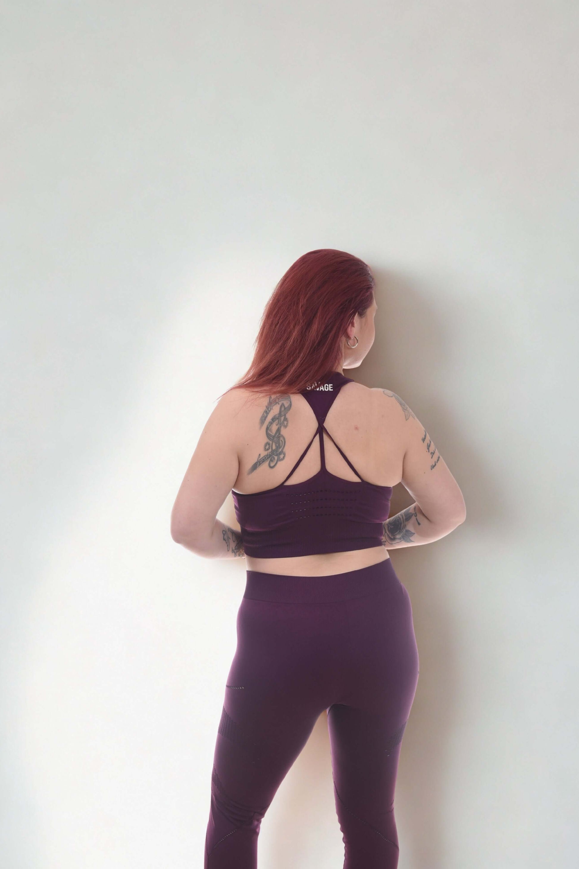 Woman wearing PERFORMANCE LEGGINGS - RAW FORGED in purple, showcasing stylish design and tattoos from a back view.